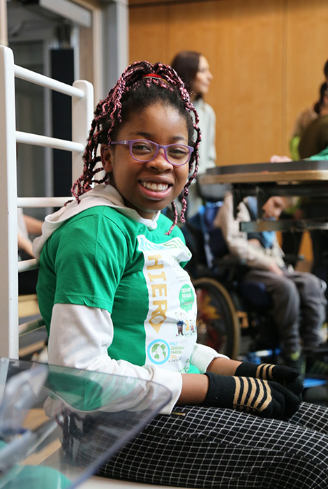 12 year old girl wearing glasses sitting on a bench and smiling at the camera.